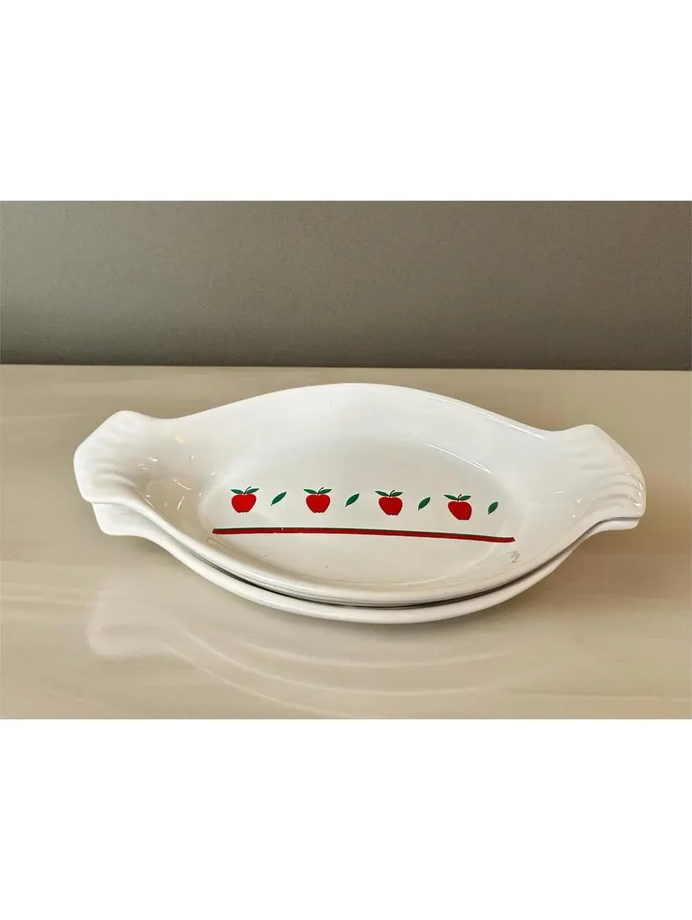 White ceramic oval au gratin dish with red apple and green leaf decoration.